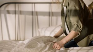 A woman wearing an olive green linen shirt, setting the linen bed sheets