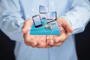 Hands holding a digital illustration of technology devices including a smartphone, computer monitors, credit card, and payment terminal, symbolizing digital solutions and modern technology services.