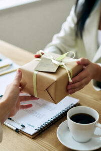 Hands exchanging a small branded gift box with thank-you note, symbolizing thoughtful gestures that build memorable client experiences.